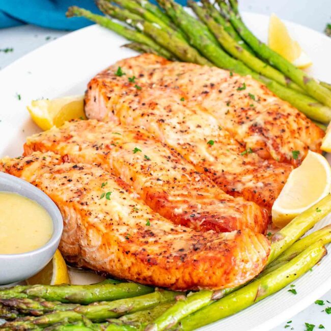 air fryer salmon and asparagus on a white platter with a lemon sauce.