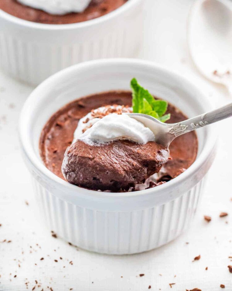 avocado chocolate mousse in a white ramekin with a spoon in it topped with whipped cream