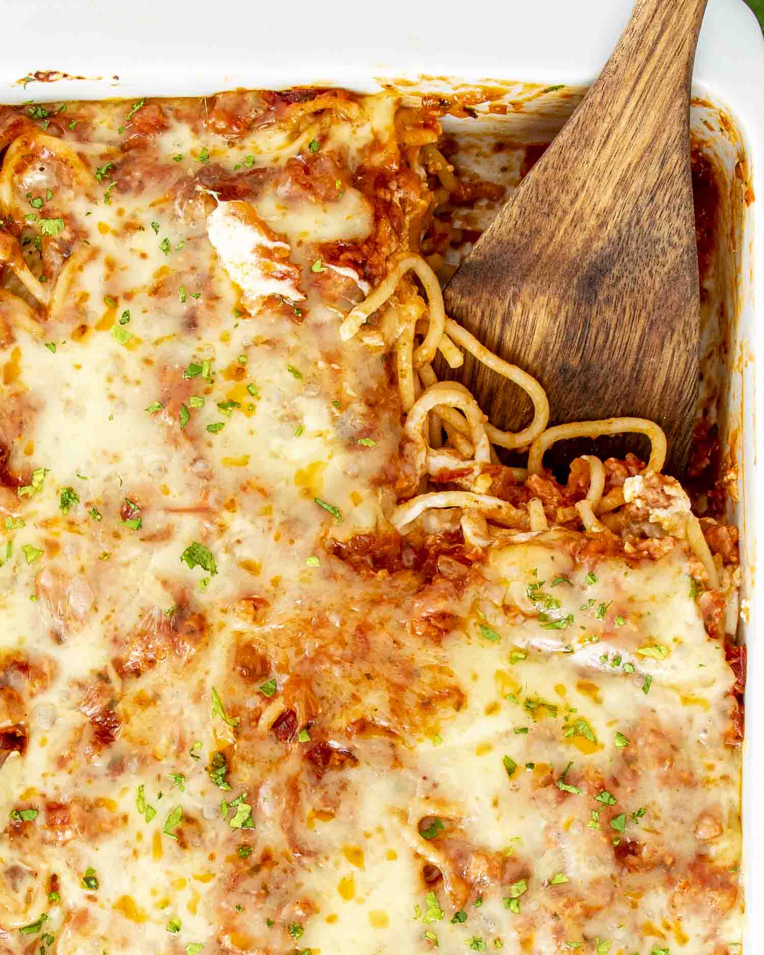 baked spaghetti garnished with parsley in a white casserole dish.