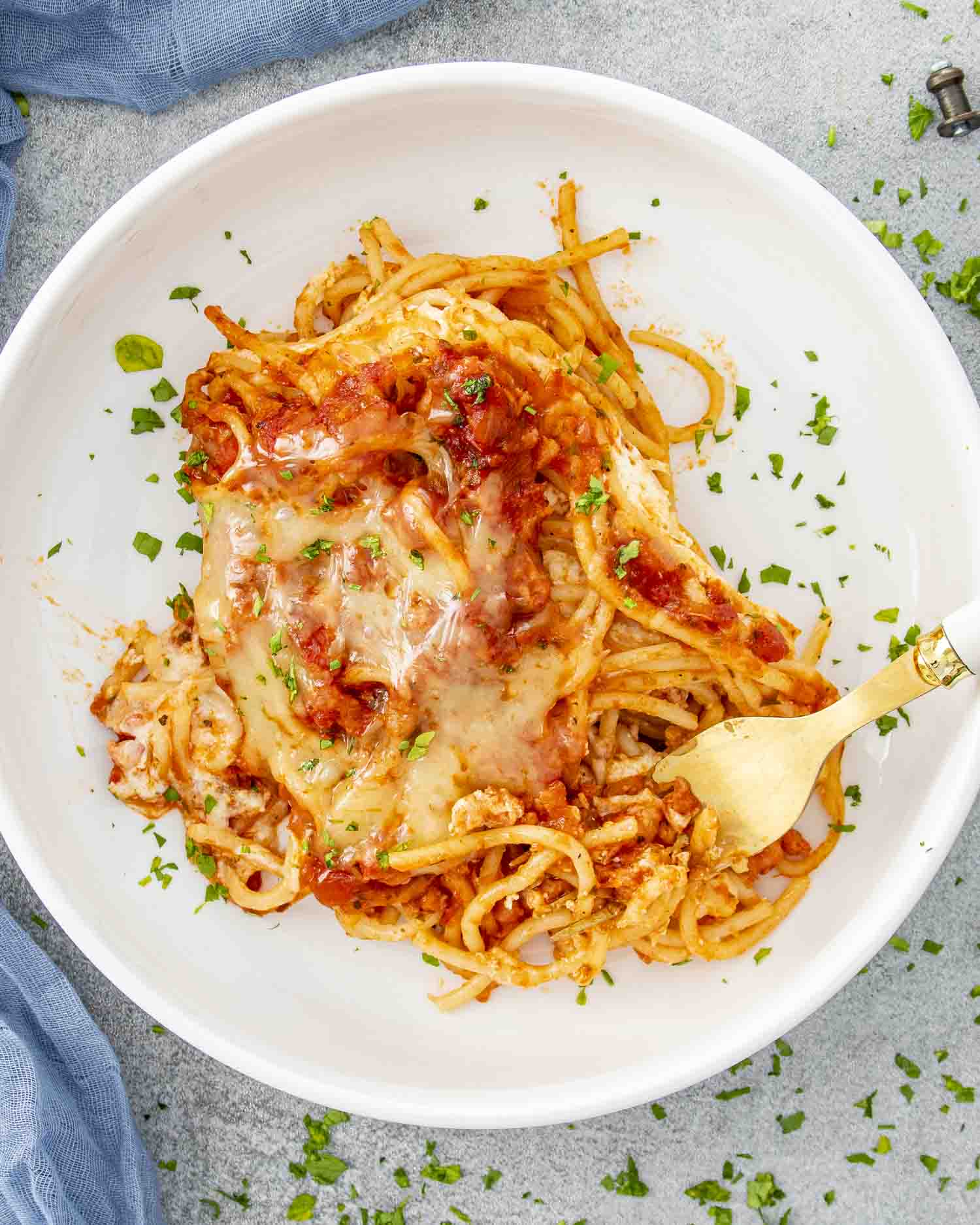 a white bowl with a serving of baked spaghetti garnished with parsley.
