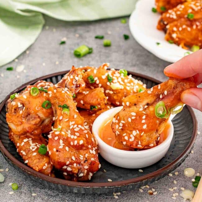 a serving of chicken wings with bang bang sauce on the side.