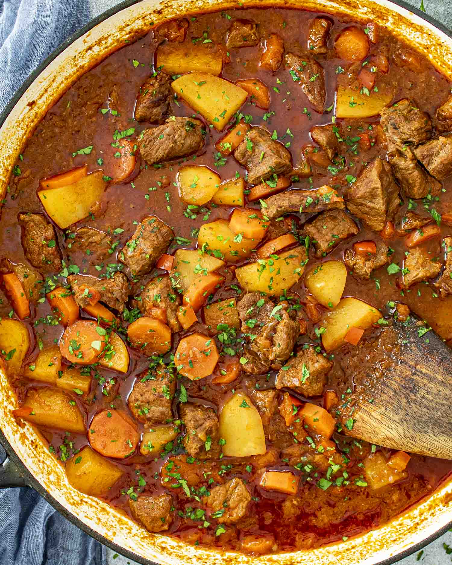 A close-up shot of a hearty Beef Goulash in a large Dutch oven. Tender chunks of beef, golden potatoes, and sliced carrots are simmered in a rich, deep-red paprika-infused broth. The dish is garnished with freshly chopped parsley, adding a pop of green.