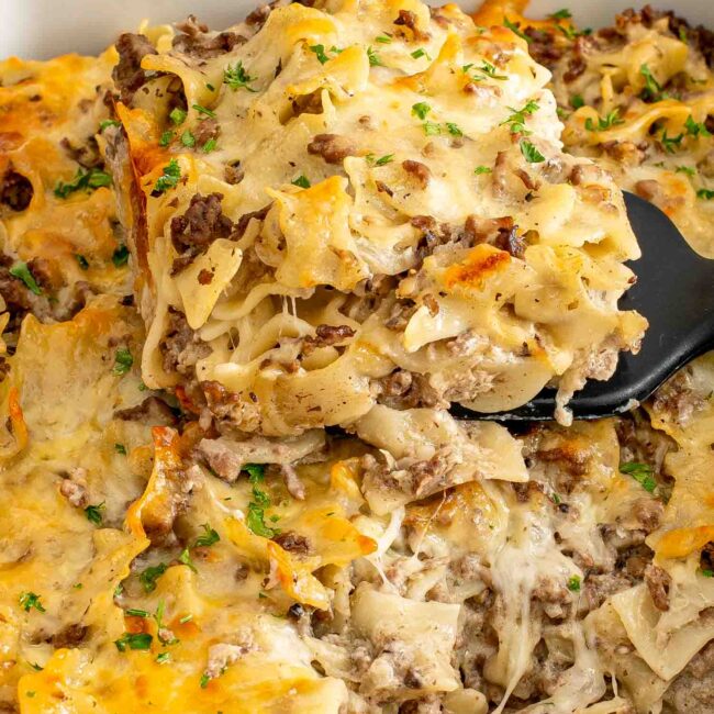 freshly baked beef stroganoff casserole in a white casserole dish garnished with parsley.