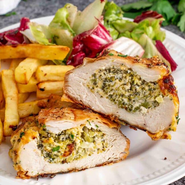 a broccoli cheese stuffed chicken breast cut in half on a plate with french fries and a salad.