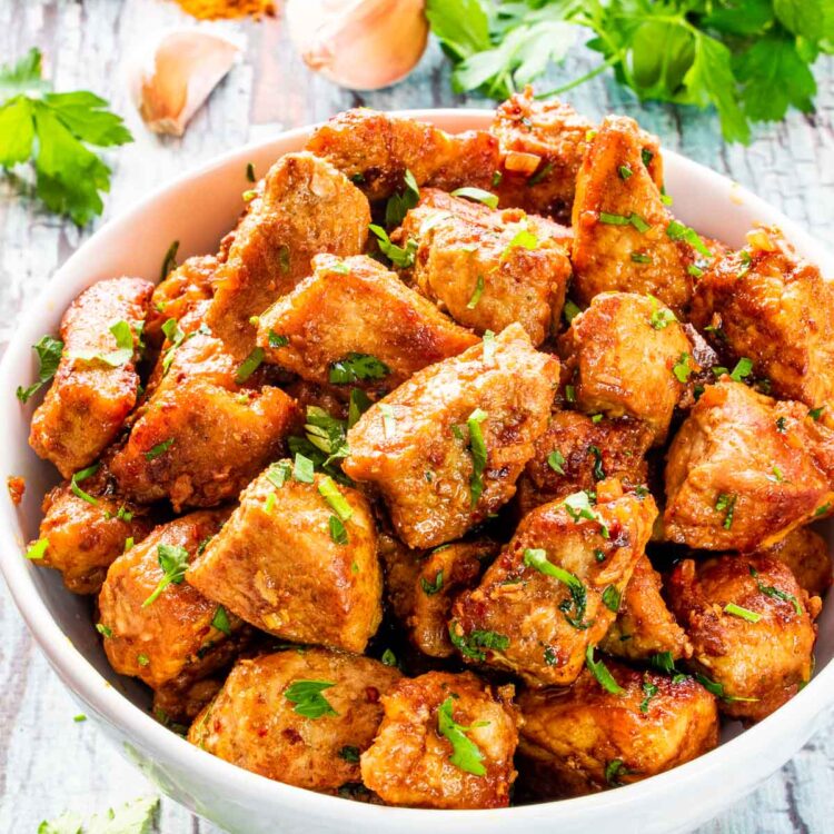 cajun pork bites garnished with parsley in a bowl.
