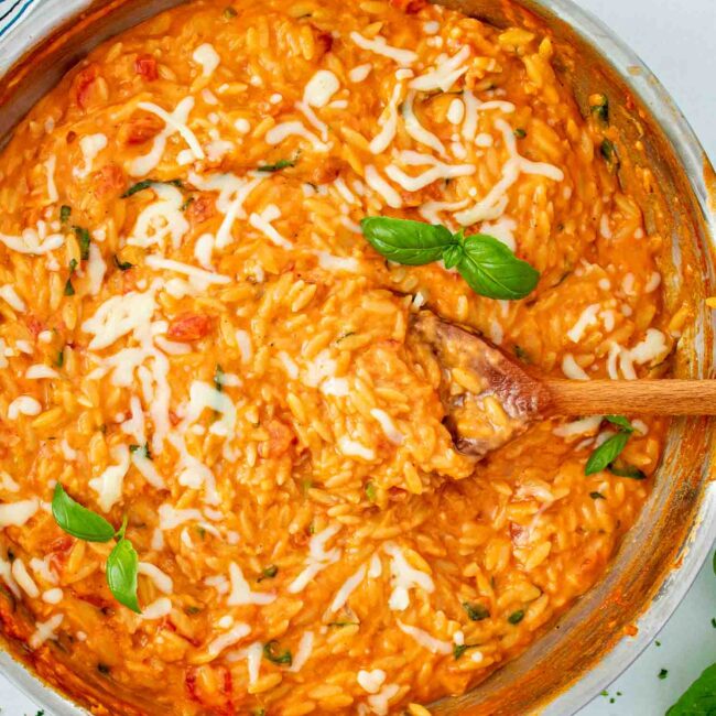 freshly made cheesy tomato basil orzo in a stainless steel skillet.