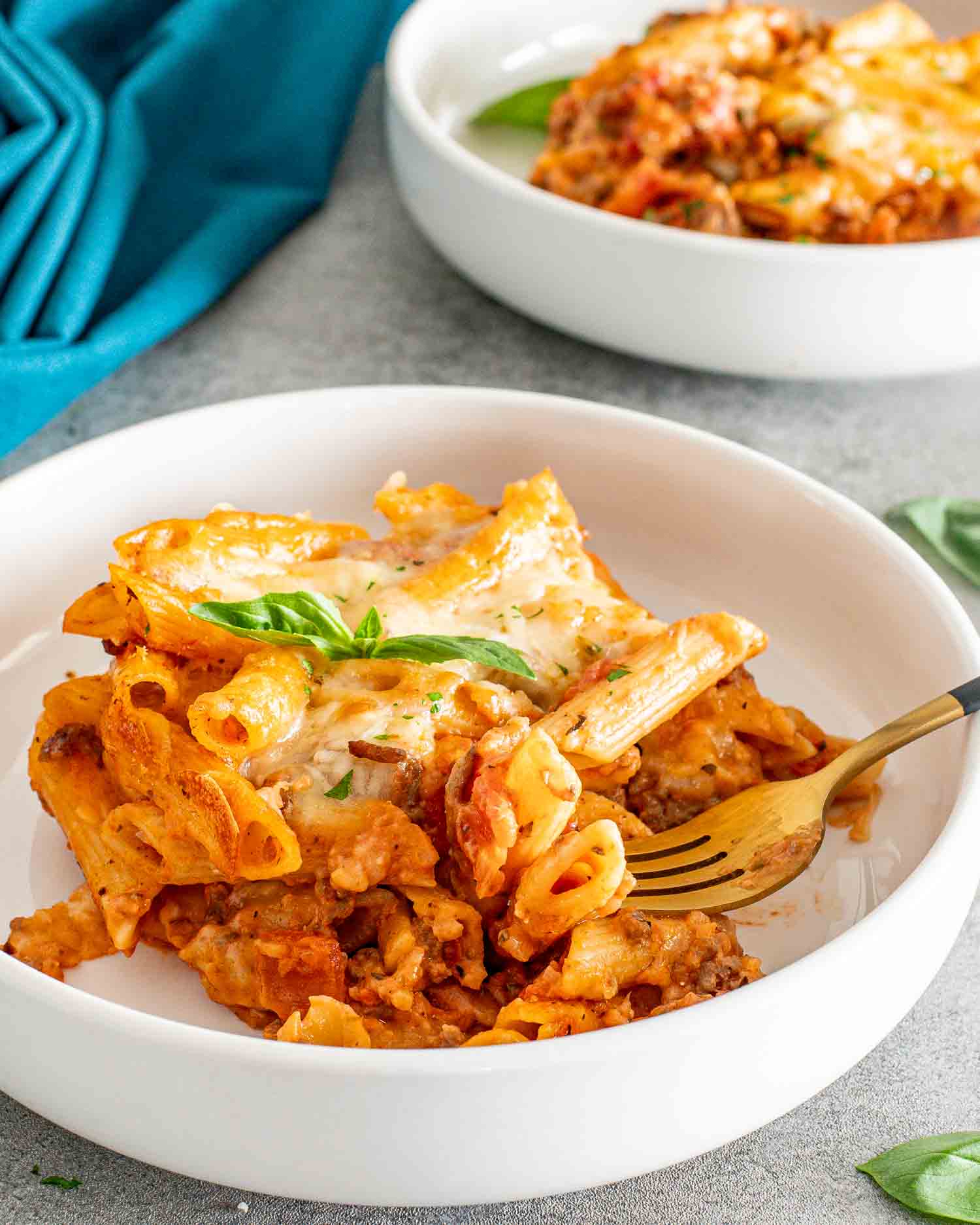 a serving of cheesy tomato beef pasta bake in a white bowl.