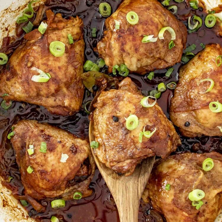 chicken adobo in a skillet garnished with green onions.