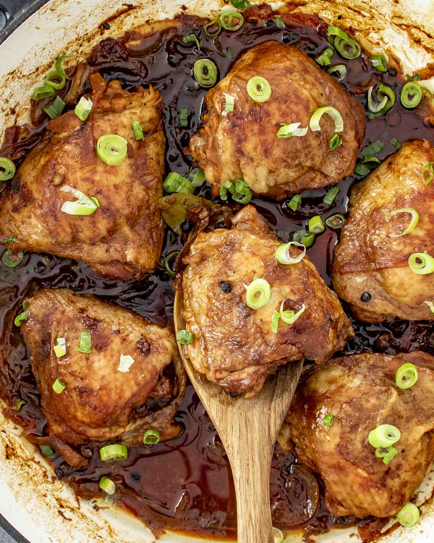 chicken adobo in a skillet garnished with green onions.
