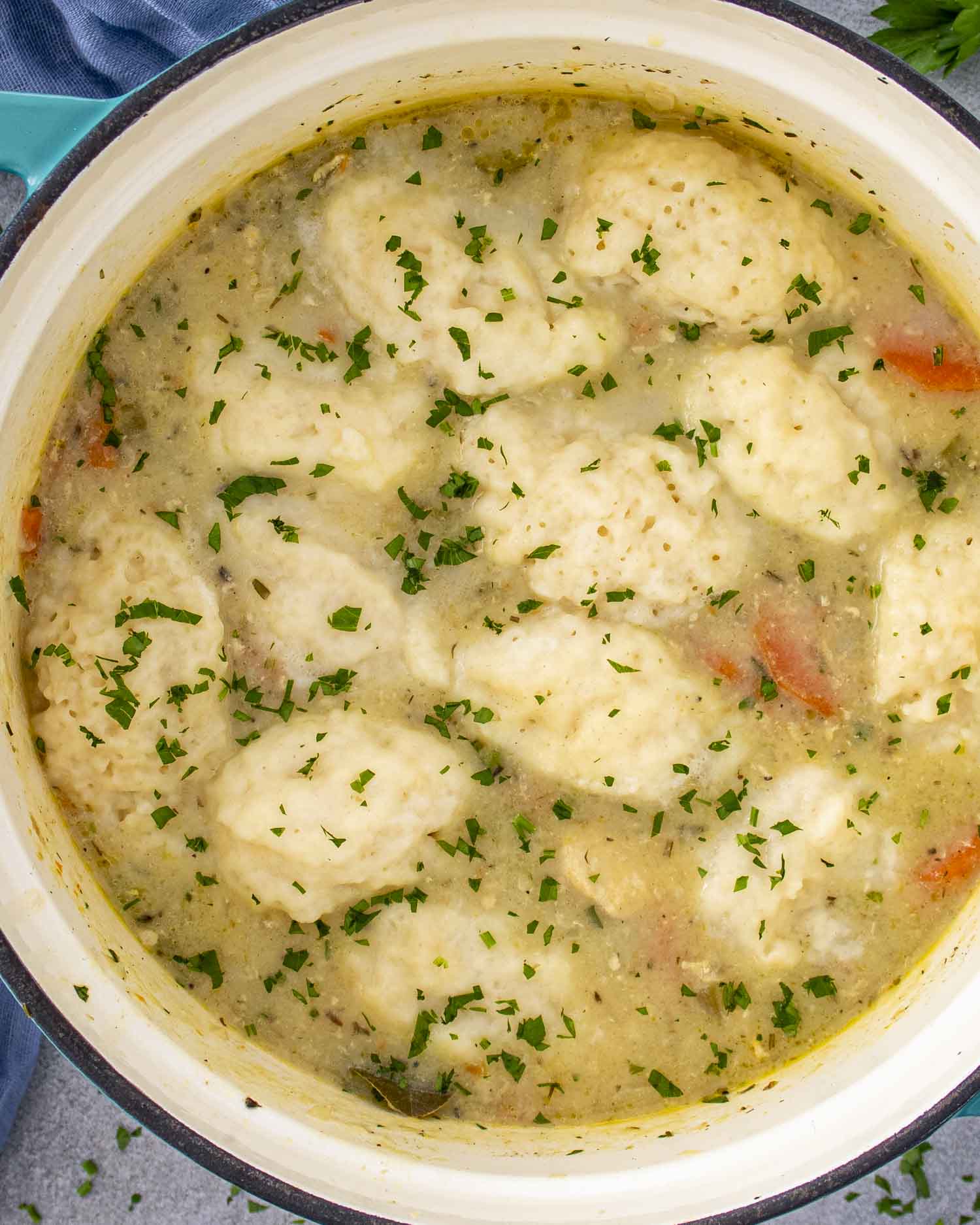 Pot of chicken and dumplings with fluffy dumplings floating in a creamy broth, garnished with parsley, ready to serve.