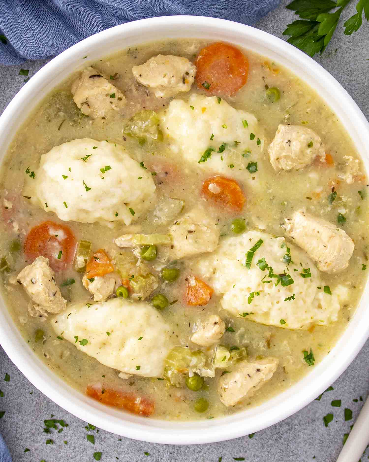 Bowl of chicken and dumplings with tender chicken, vegetables, and fluffy dumplings in a creamy broth, garnished with parsley.