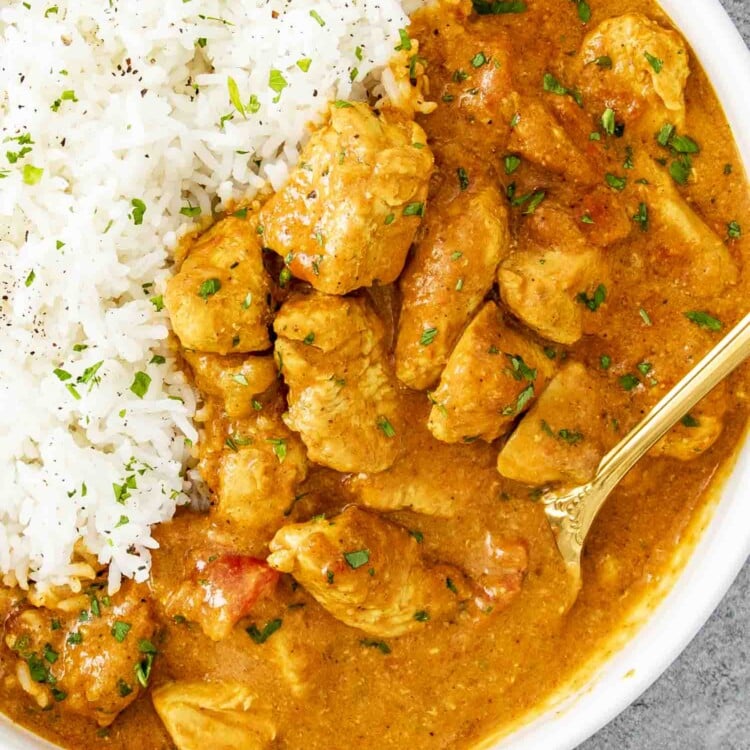 chicken curry in a white serving bowl along some cooked rice garnished with cilantro.