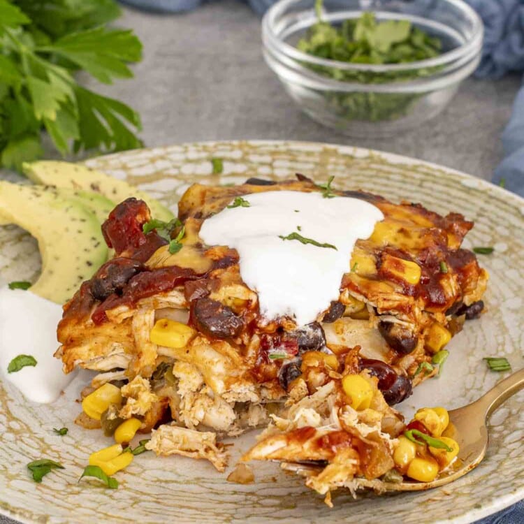 a slice of chicken enchilada casserole on a plate with a dollop of sour cream.