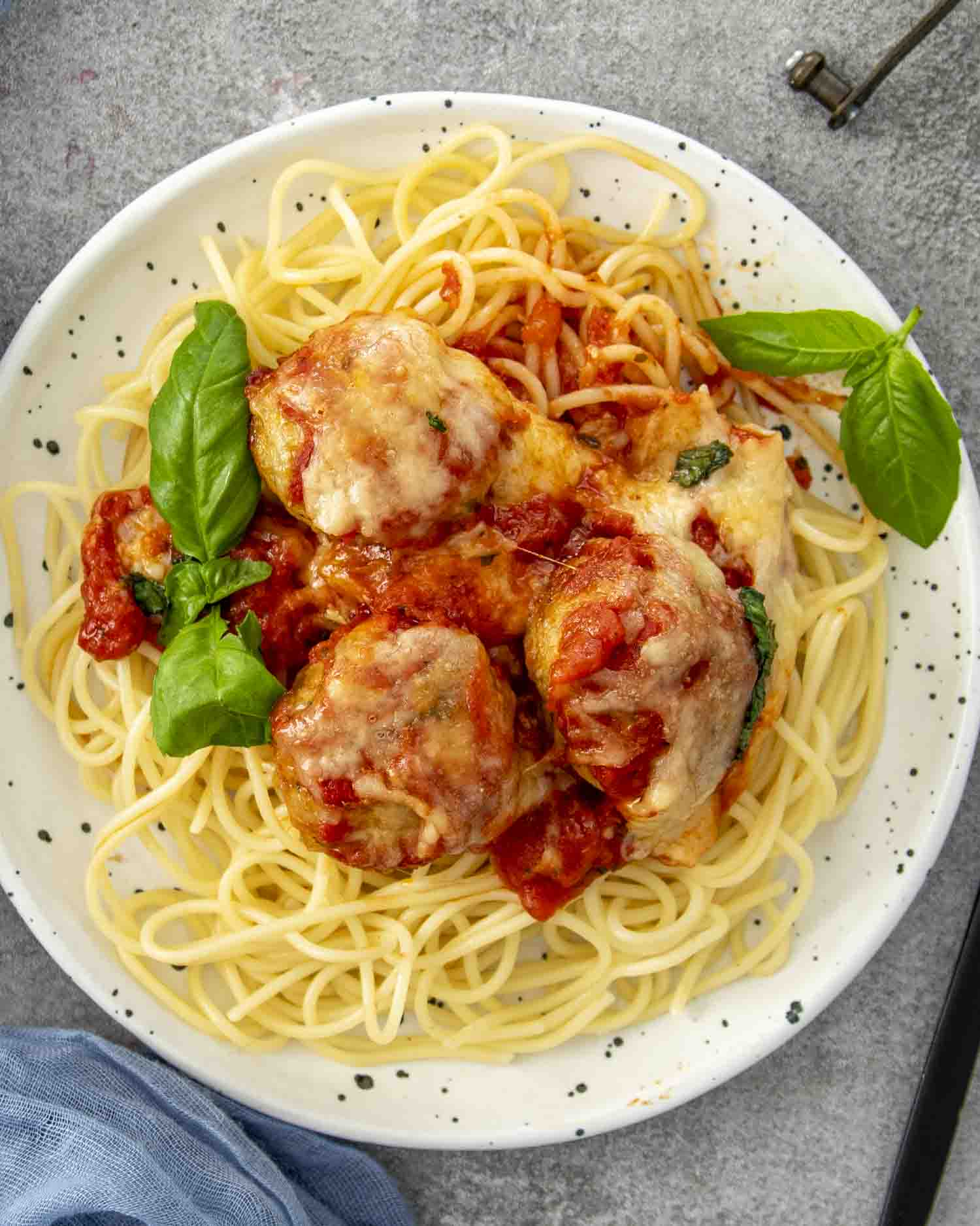 a serving of chicken parmesan meatballs on a bed of spaghetti garnished with some fresh basil.