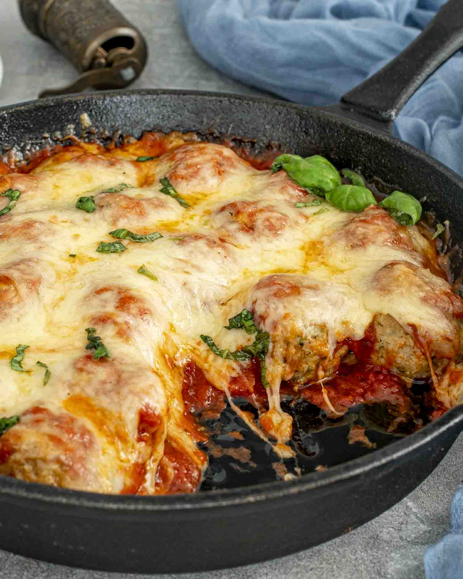 fresh out of the oven chicken parmesan meatballs in a cast iron skillet garnished with some fresh basil.