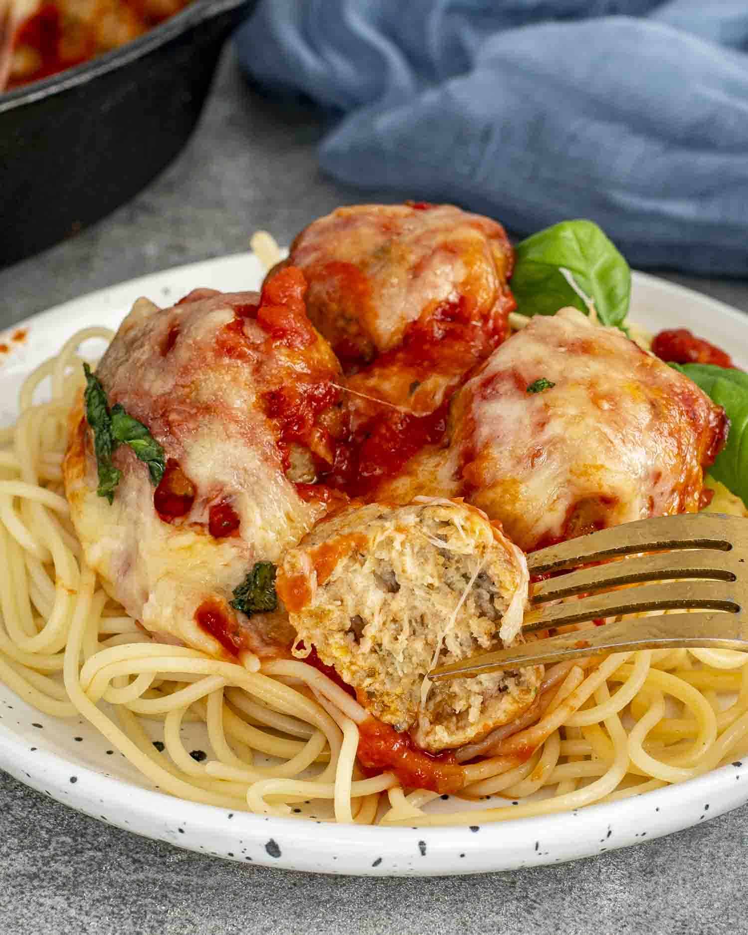 a serving of chicken parmesan meatballs on a bed of spaghetti garnished with some fresh basil.