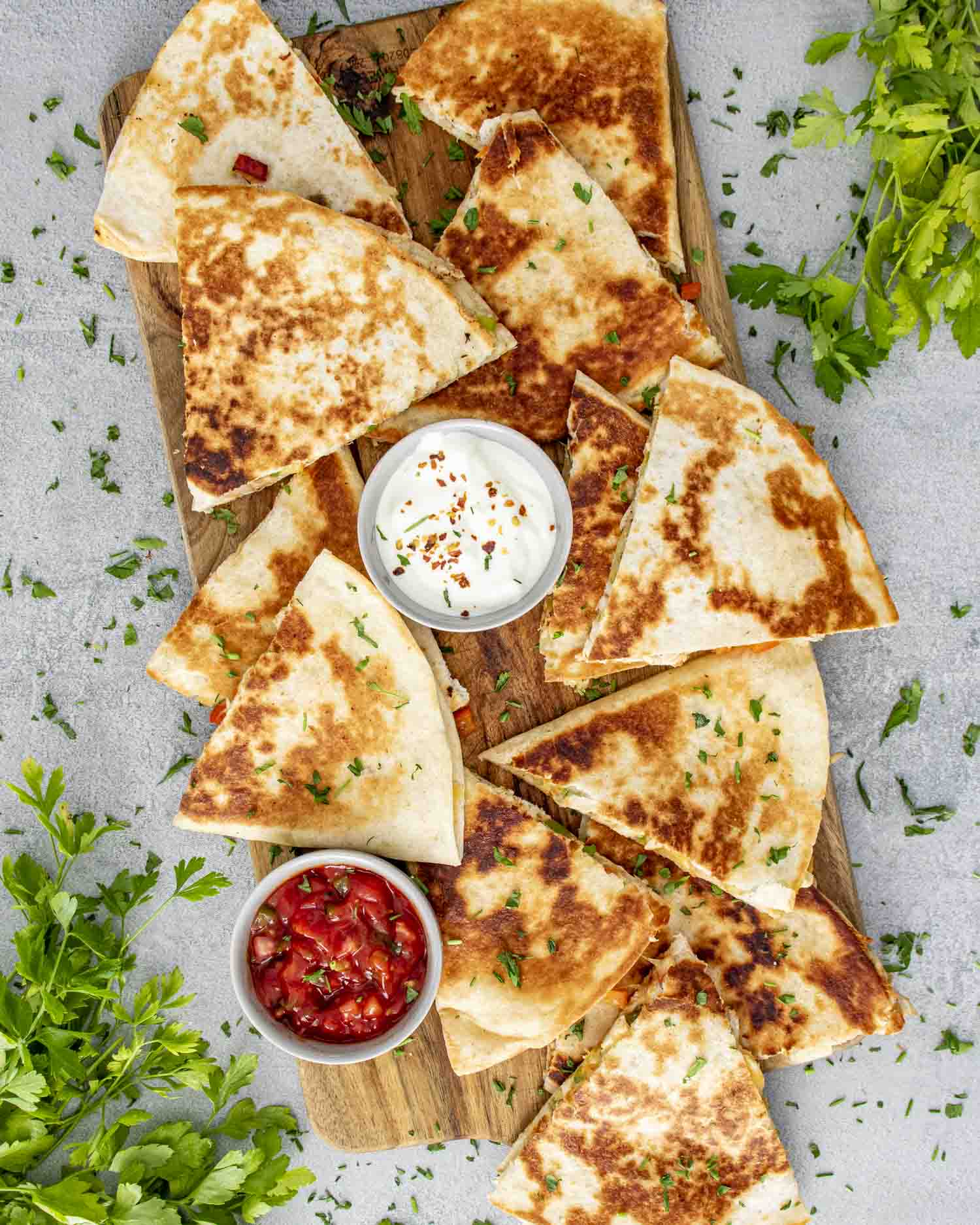 chicken quesadillas on a cutting board with two little bowls filled with salsa and sour cream.