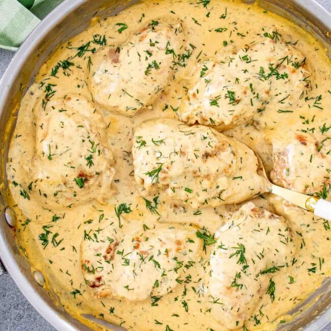 chicken thighs with creamy lemon dill sauce in a skillet with a spoon.