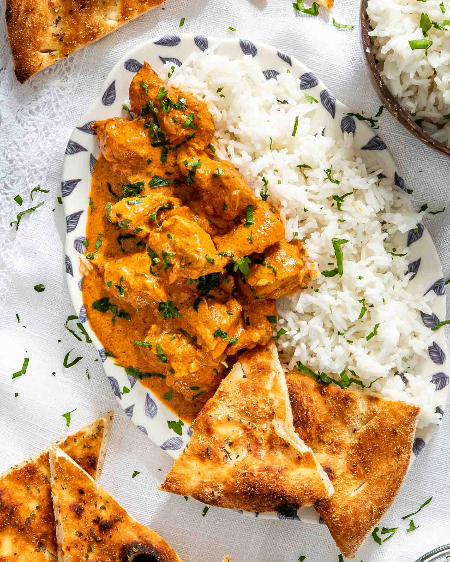 chicken tikka masala with rice in a white bowl and a piece of naan.