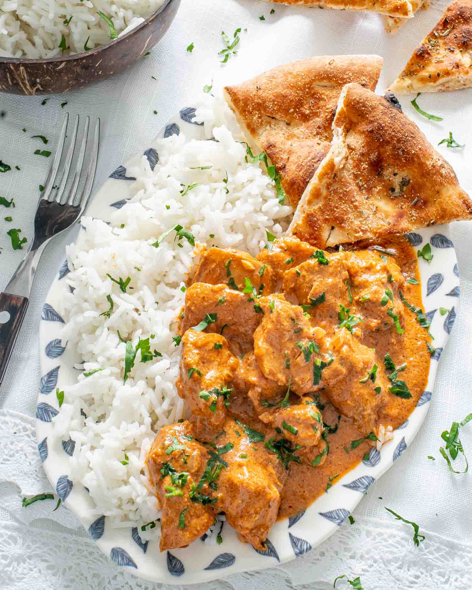 chicken tikka masala with rice in a white bowl and a piece of naan.
