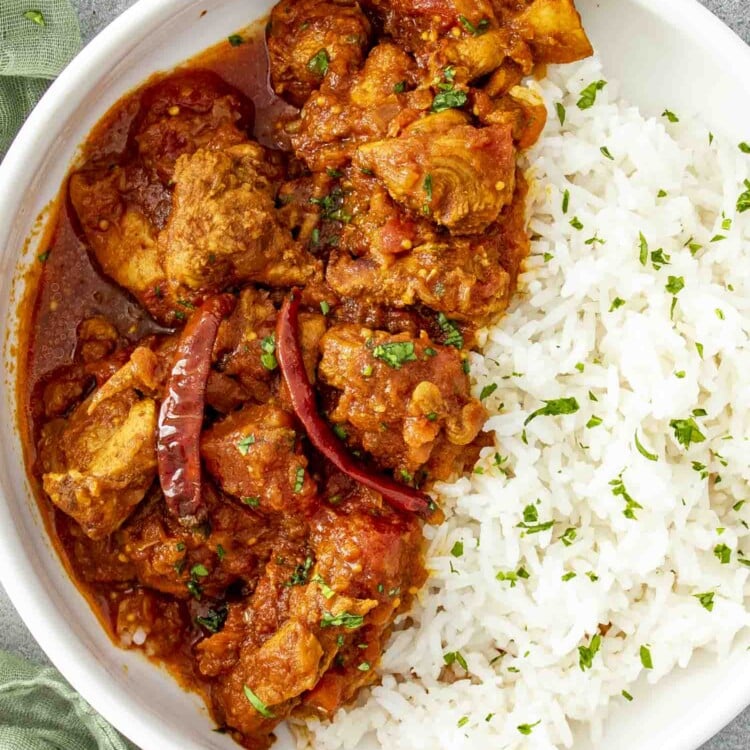 a serving of chicken vindaloo with rice in a white plate.