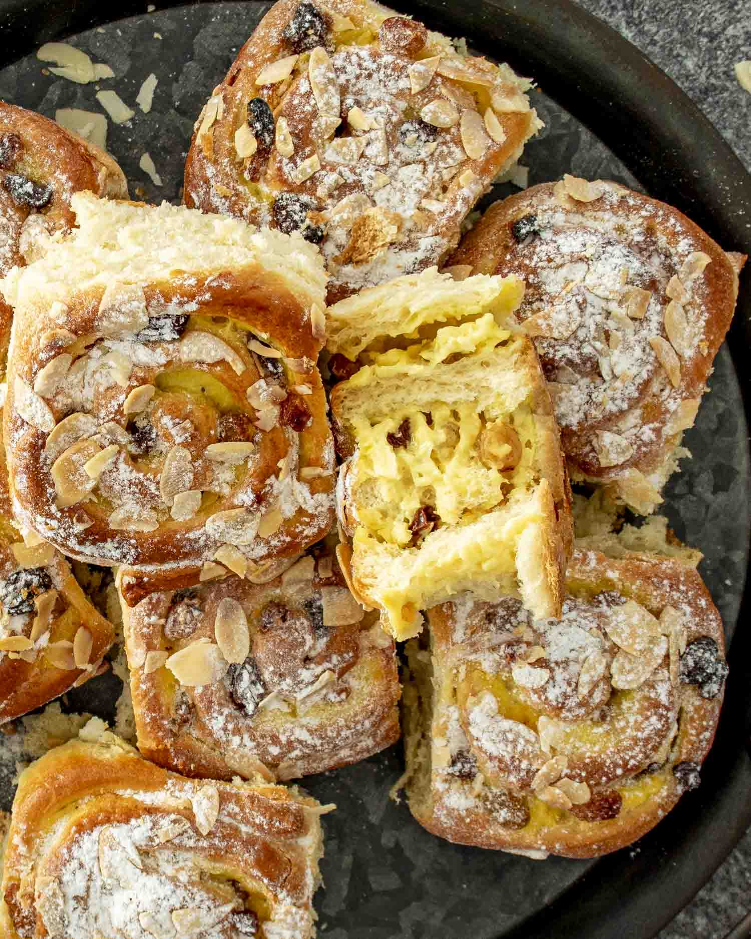 a few custard raisin rolls on a dark plate, dusted with icing sugar.