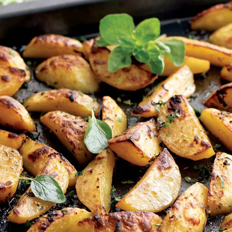 fresh out of the oven greek lemon potatoes on a baking sheet garnished with fresh oregano