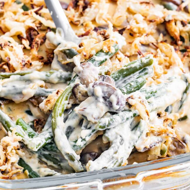 a serving spoon full of green bean casserole in a casserole dish.