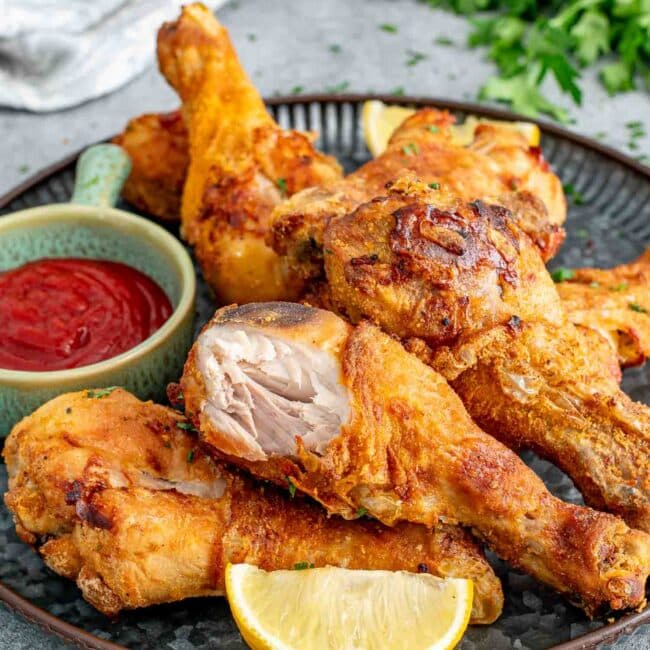 a plateful of homemade shake n' bake chicken made in the air fryer on a metal plate with some ketchup.