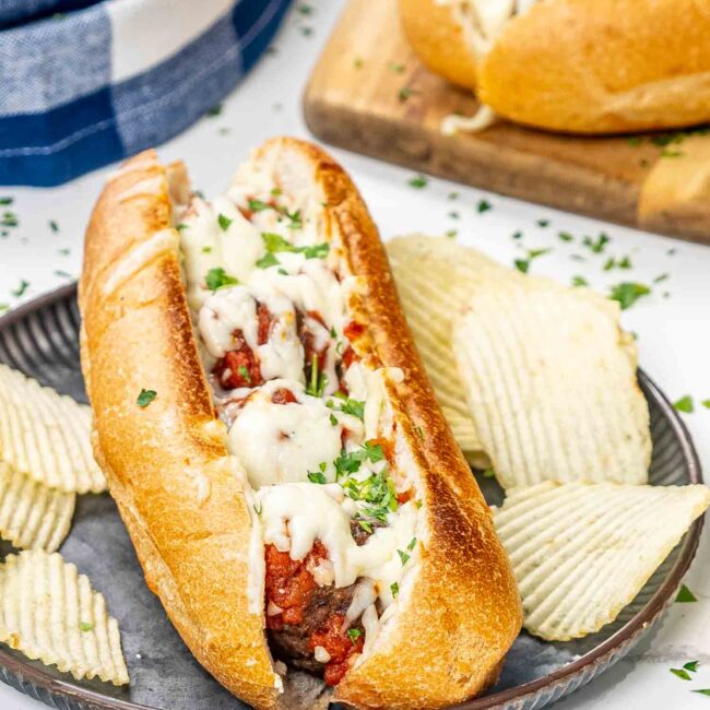 a meatball sub garnished with parsley with potato chips on a plate.