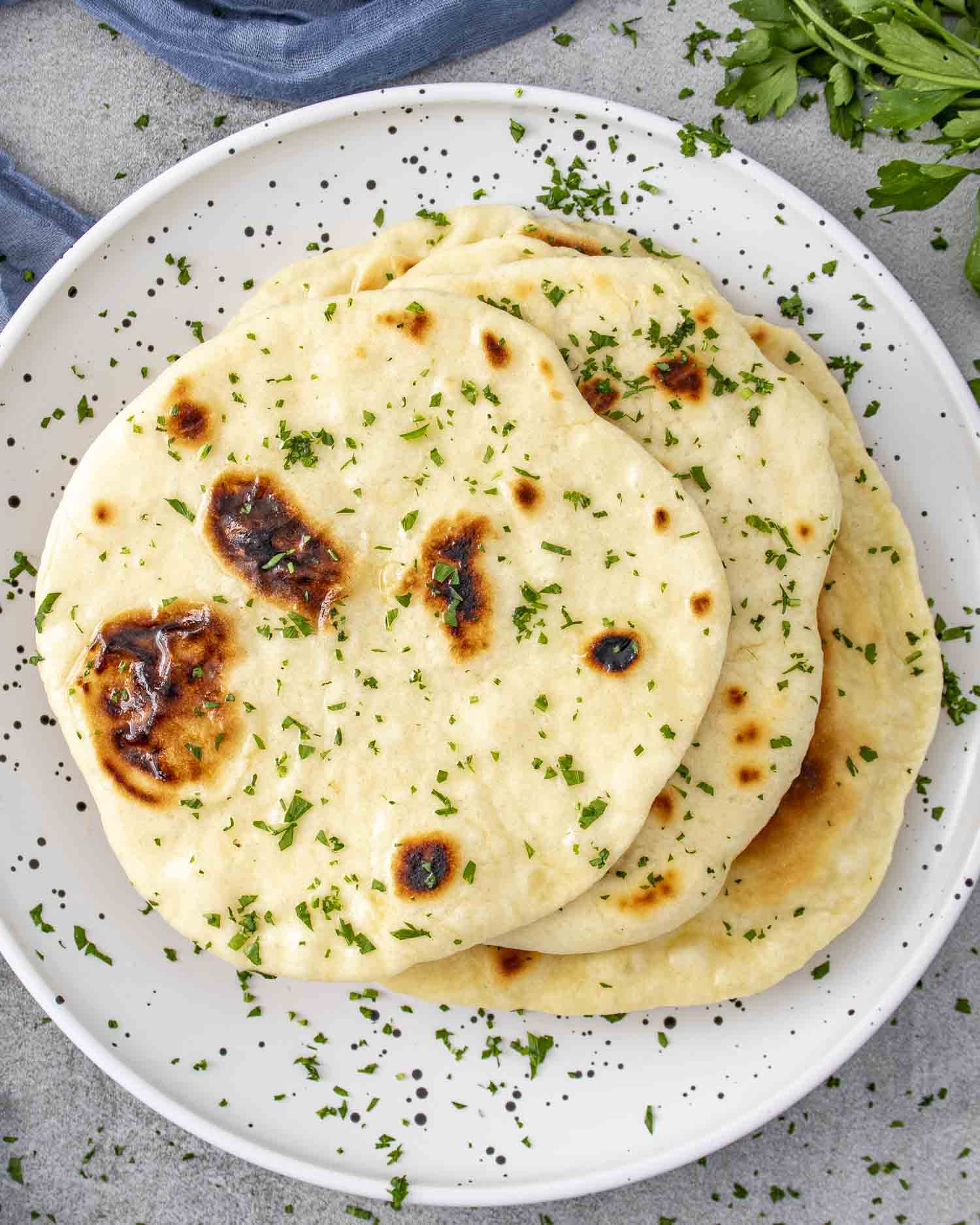 a few naan on a plate, brushed with butter and garnished with parsley.