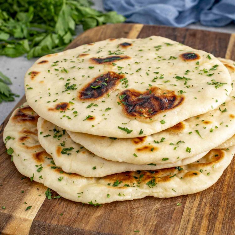 a few scattered naan on a cutting board, brushed with butter and garnished with parsley.