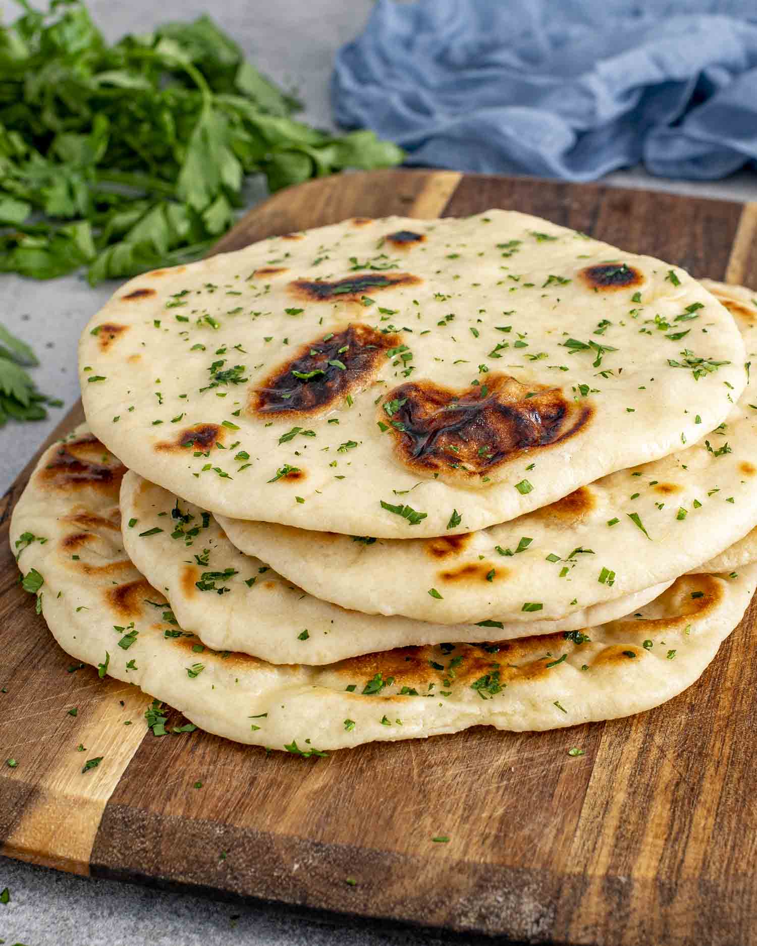 a few scattered naan on a cutting board, brushed with butter and garnished with parsley.