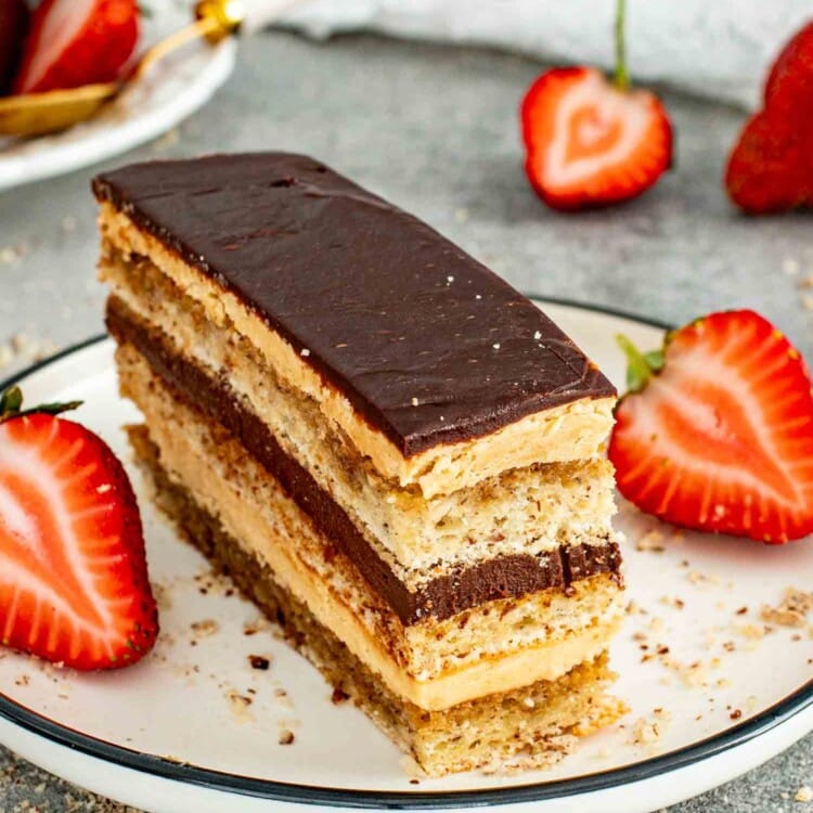 a gorgeous slice of opera cake on a white plate garnished with strawberries.