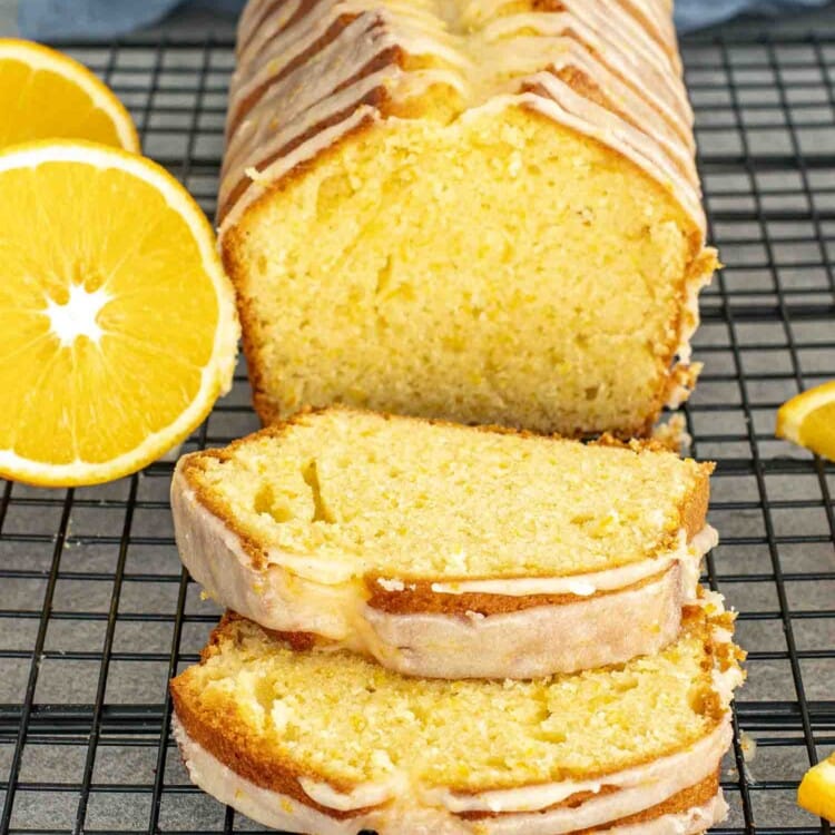 A freshly baked orange cake sliced into thick pieces, drizzled with orange glaze, and resting on a black cooling rack.