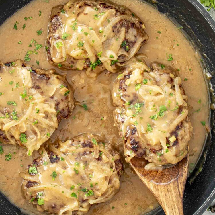 Juicy beef patties covered in rich, creamy onion gravy, garnished with fresh parsley, served hot in a black skillet.