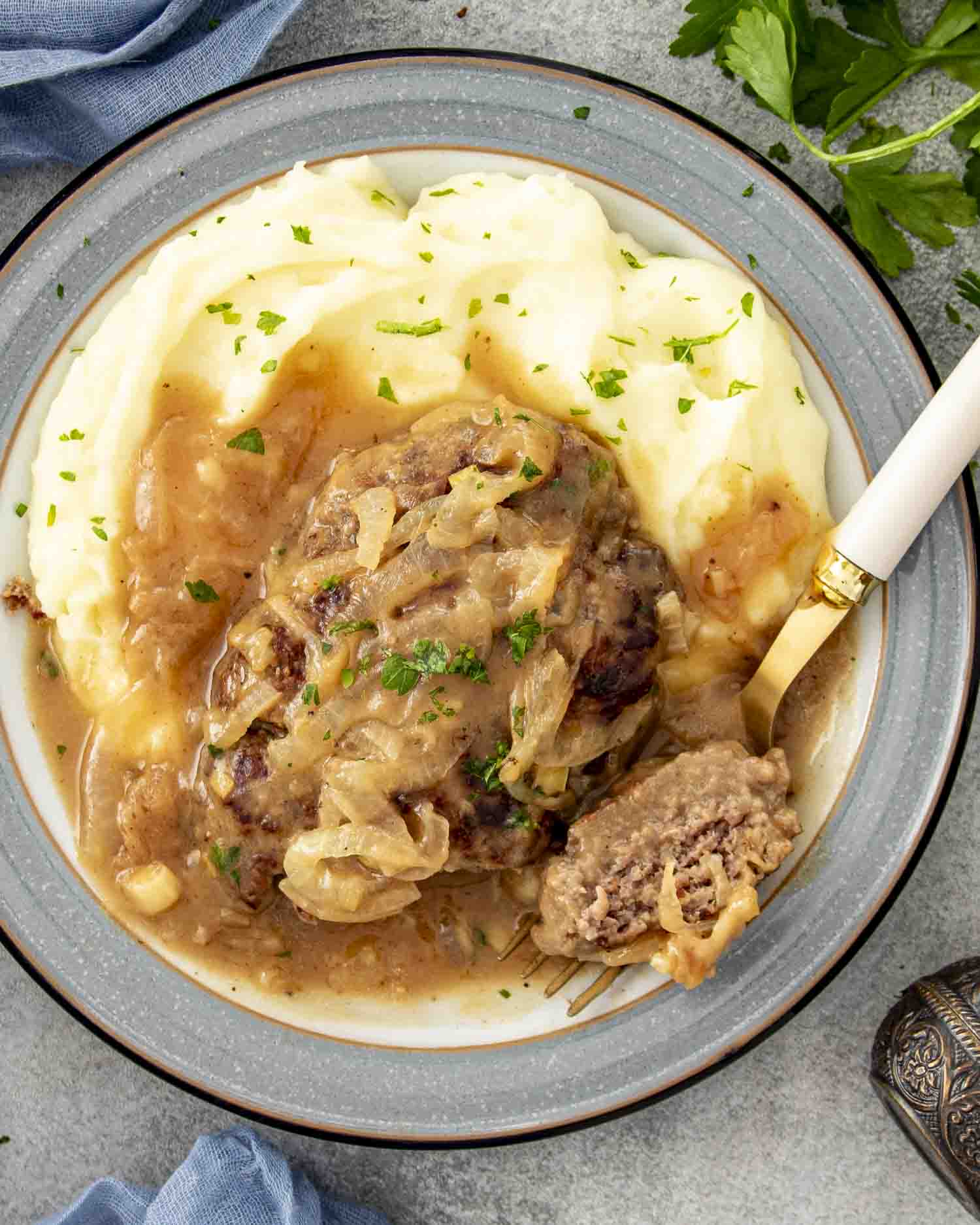 Poor man's steak served with creamy mashed potatoes and savory onion gravy on a plate, garnished with chopped fresh parsley.
