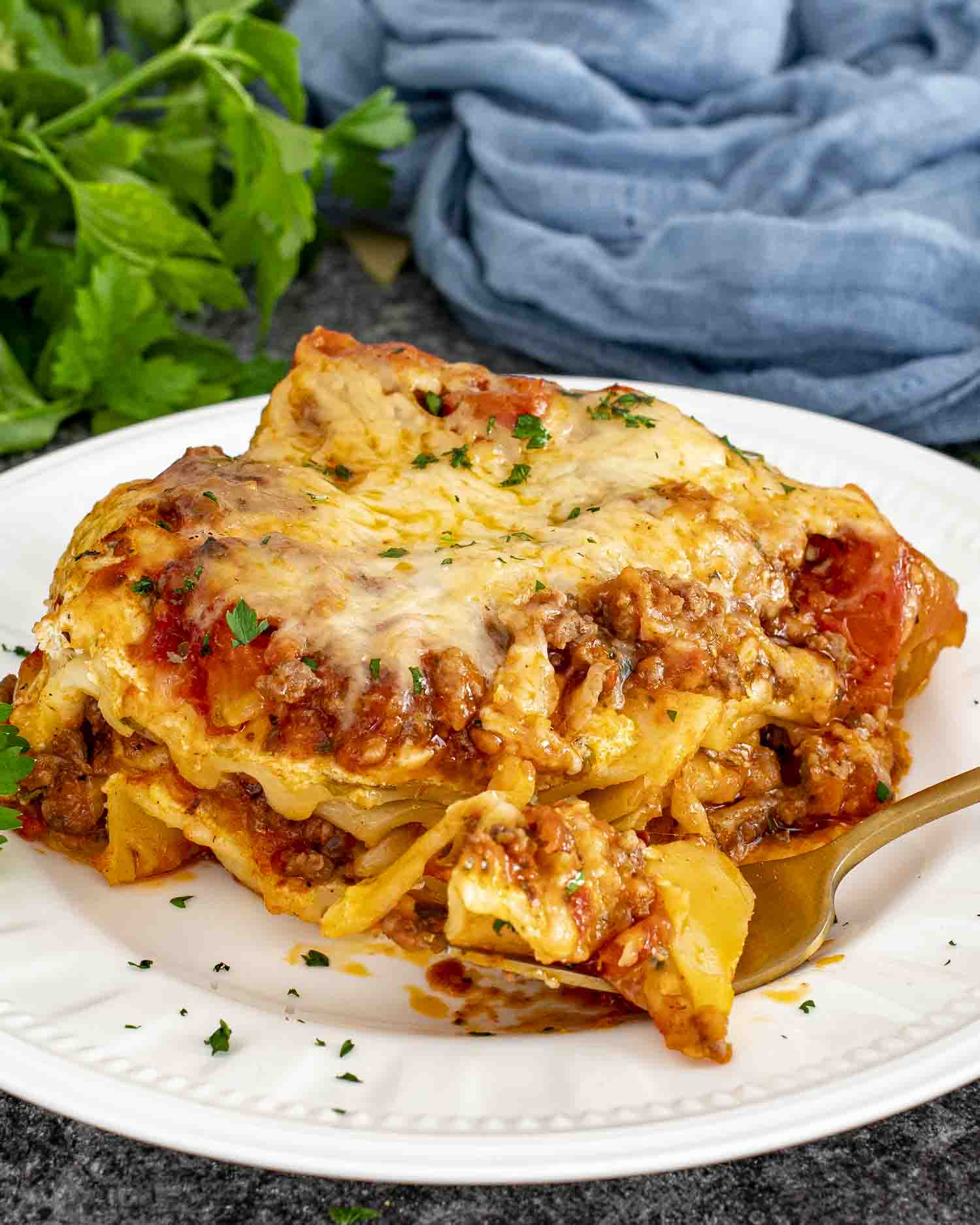 a slice of lasagna on a white plate garnished with a bit of parsley.