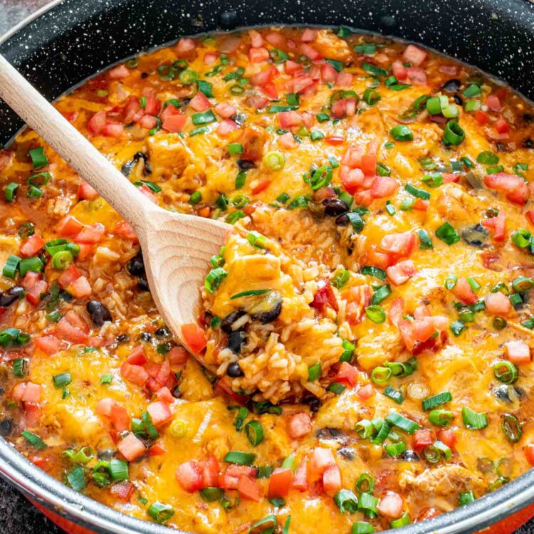 southwest chicken and rice in a skillet with a wooden spoon inside.