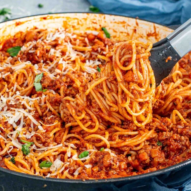 freshly made spaghetti bolognese in a pot garnished with basil and parmesan cheese.