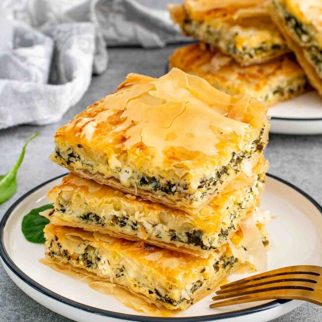 Stacked spanakopita slices on a plate with a fork, ready to eat.