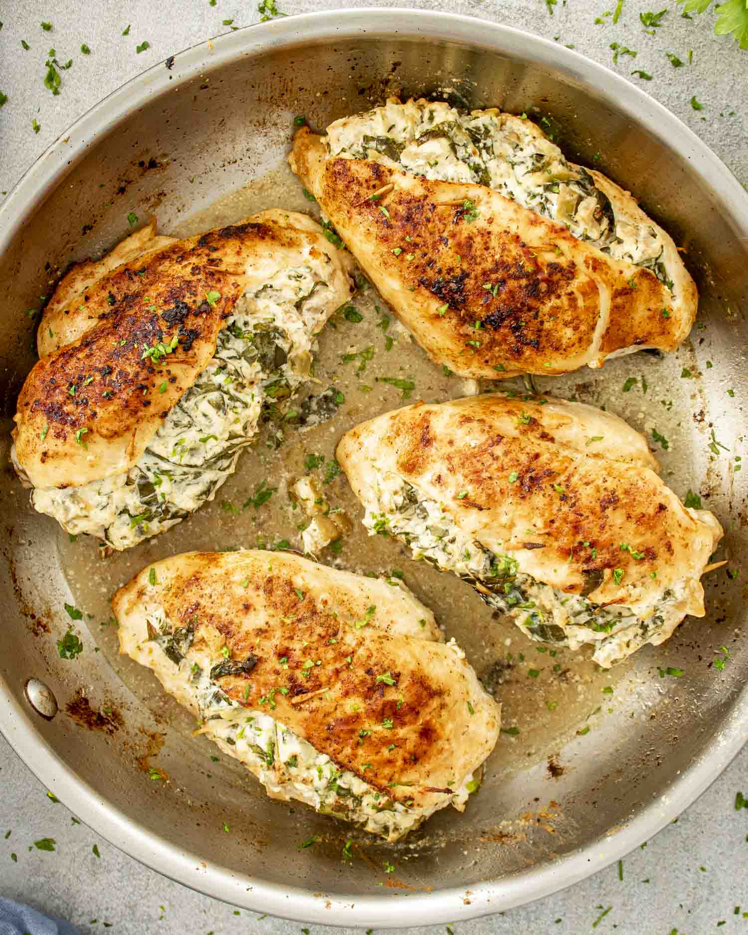 Golden-brown chicken breasts stuffed with a creamy spinach and artichoke filling, served in a stainless steel skillet, garnished with parsley.