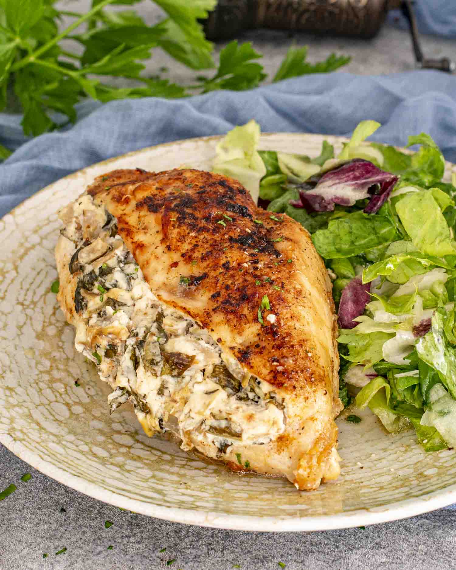 A stuffed chicken breast with a creamy spinach and artichoke filling, served with a fresh green salad on a speckled plate.