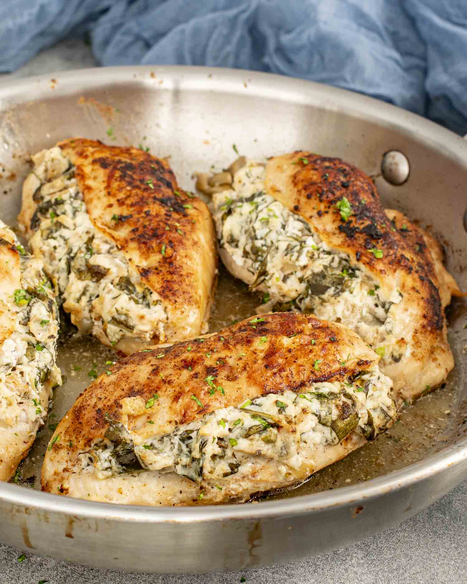 Golden-brown chicken breasts stuffed with a creamy spinach and artichoke filling, served in a stainless steel skillet, garnished with parsley.