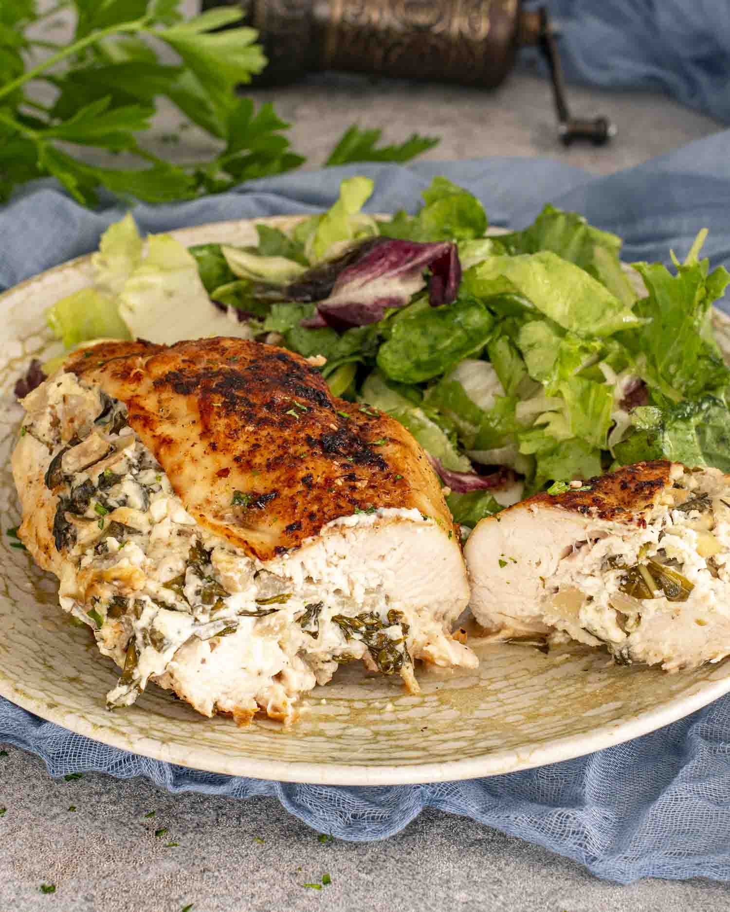 A golden spinach and artichoke stuffed chicken breast sliced in half, served with a mixed green salad on a patterned plate.