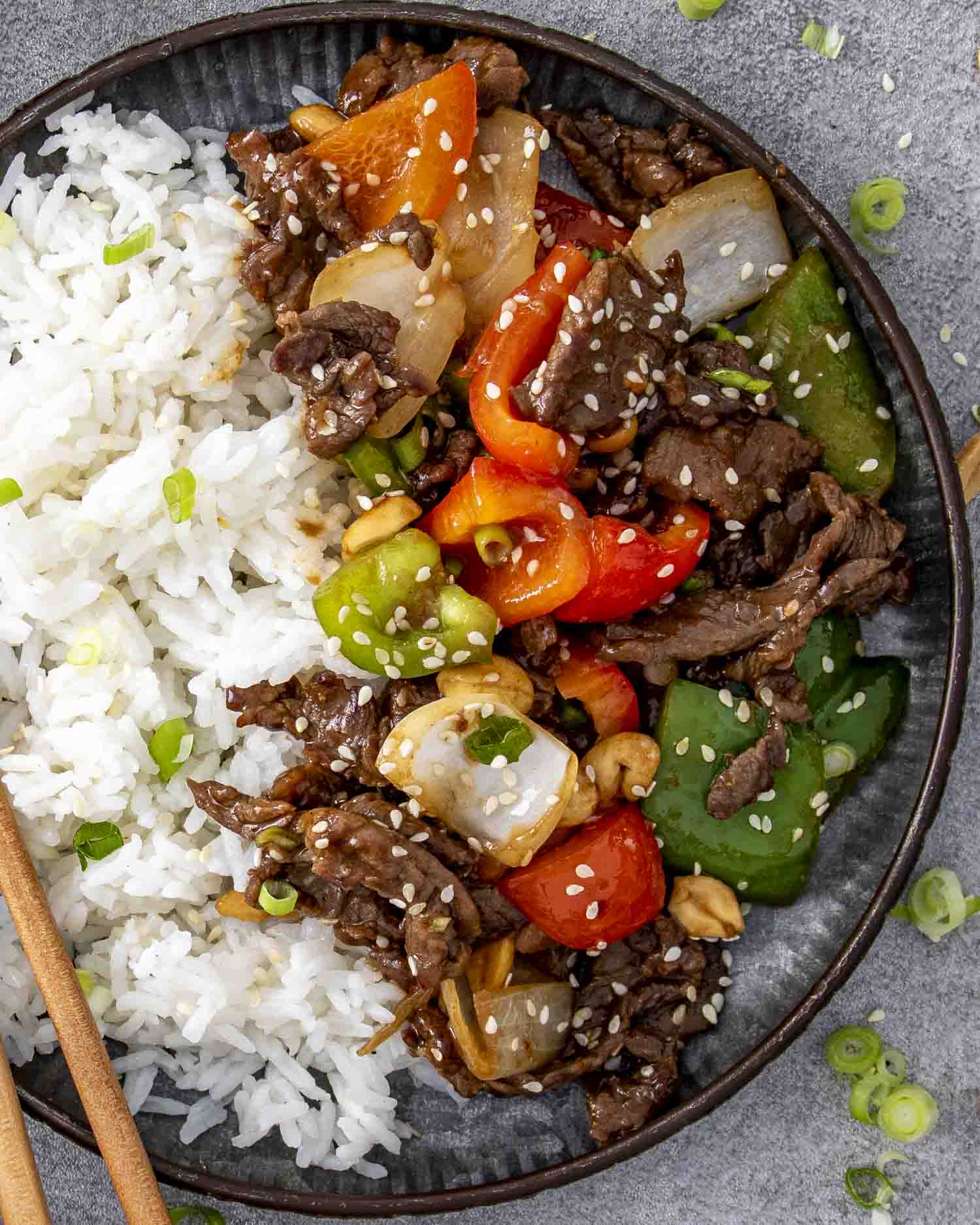 szechuan beef with rice on a plate garnished with sesame seeds.