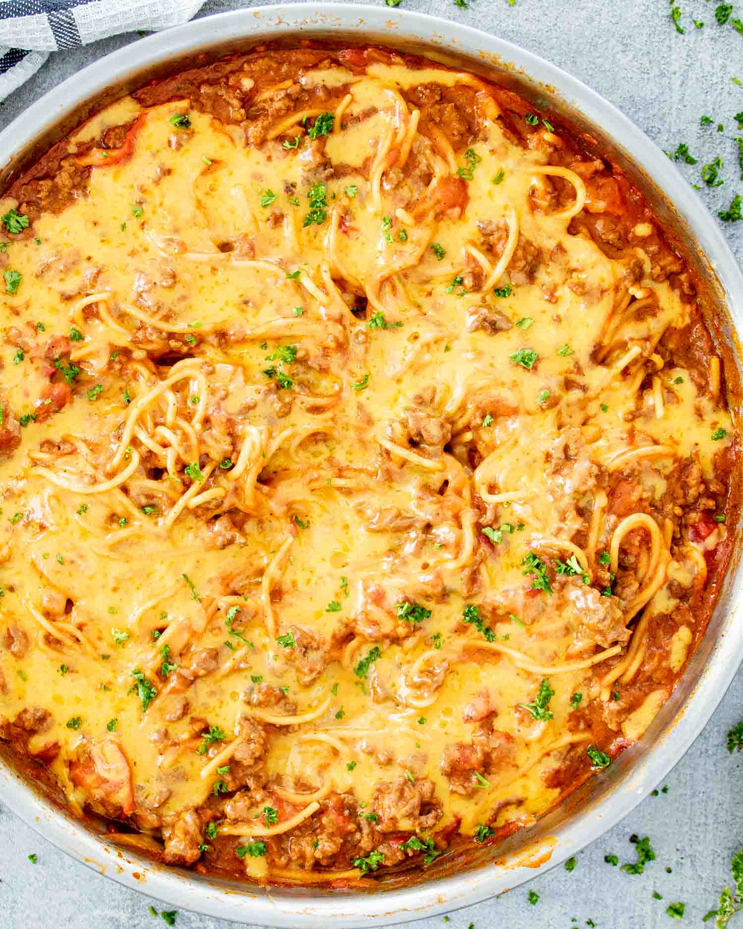 freshly made taco spaghetti in a stainless steel skillet topped with cheese and garnished with parsley.