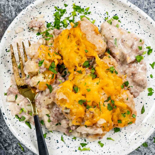a serving of tater tot casserole on a white dish with a fork and garnished with parsley.
