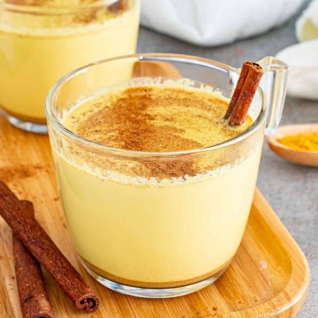 A warm turmeric latte garnished with a dusting of cinnamon and a whole cinnamon stick.