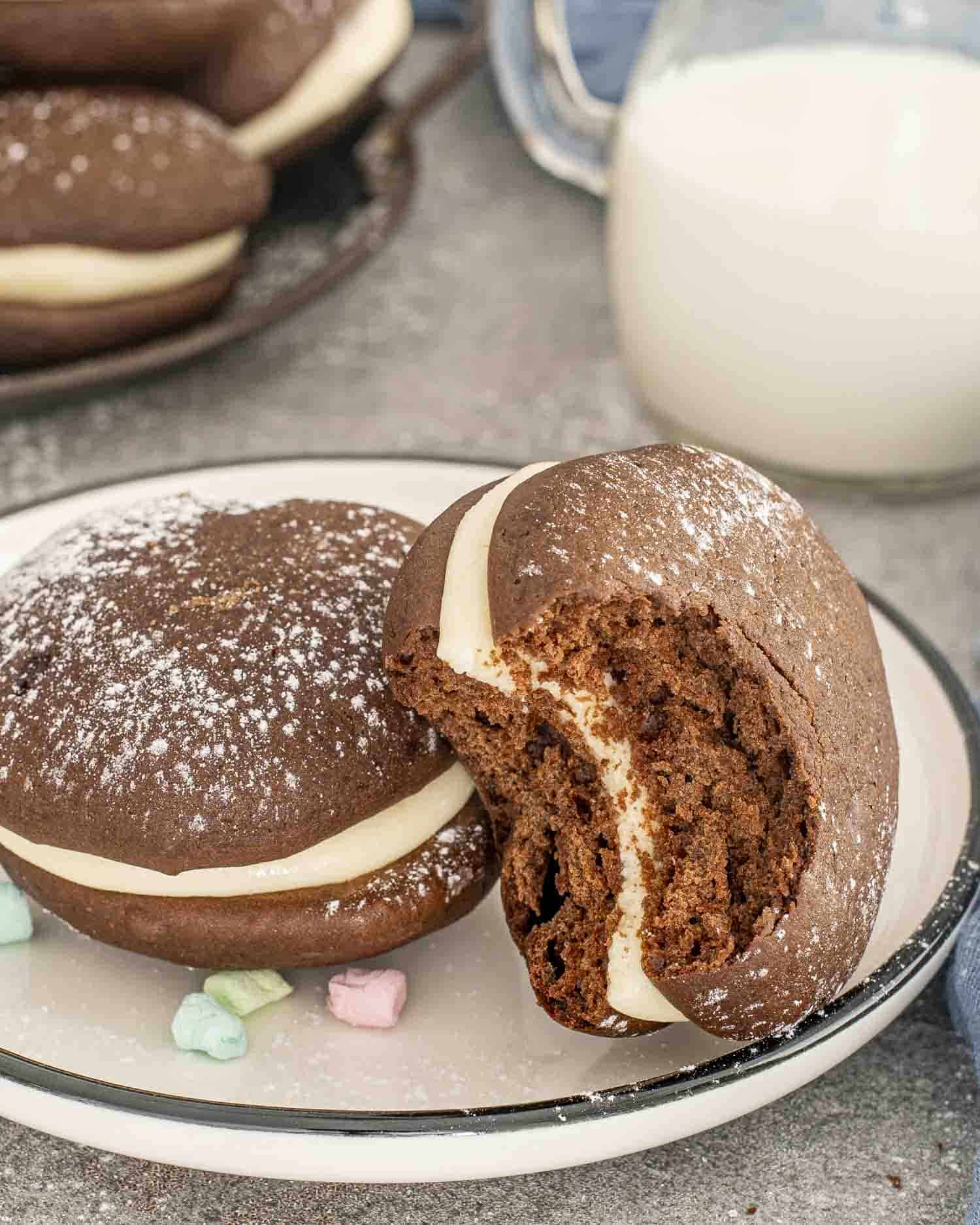 two whoopie pies on a plate with one having a bite taken out of it.